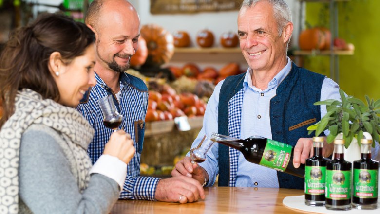 Wurzers, © Daniel Schalhas Drei Personen bei einer Weinverkostung in einem Geschäft mit Kürbissen im Hintergrund.