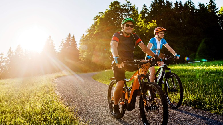 Radfahren entlang der Moststraße, © Mostviertel Tourismus/schwarz.koenig.at Zwei Personen fahren bei Sonnenuntergang auf E-Bikes auf einem Weg durch eine grüne Landschaft.
