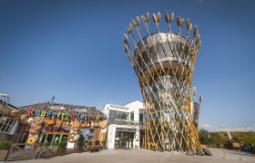 Ein modernes Gebäude mit einem Turm, der von Weizenähren umgeben ist, neben einem dekorativen Knusperhäuschen.