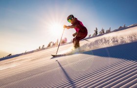 Skifahrer fährt bei Sonnenaufgang auf einer frisch präparierten Piste bergab.