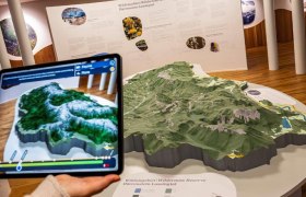 Ein Tablet zeigt eine digitale Karte über einem physischen 3D-Modell einer Landschaft im Haus der Wildnis.