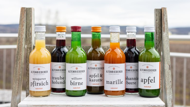 Verschiedene Flaschen mit Fruchts&auml;ften von Altenriederer auf einem Regal im Freien.