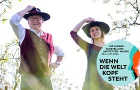 Zwei Personen mit Hüten in einem blühenden Garten, Plakat für NÖ Landesausstellung 2026.