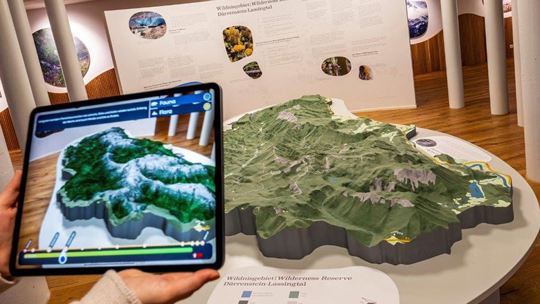 Ein Tablet zeigt eine digitale Karte über einem physischen 3D-Modell einer Landschaft im Haus der Wildnis.