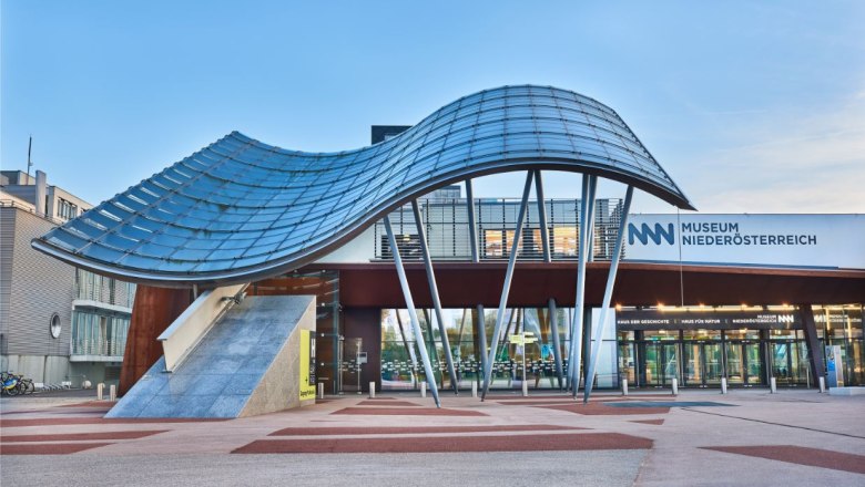 Eingang des Museums Niederösterreich mit moderner Architektur und geschwungenem Glasdach.