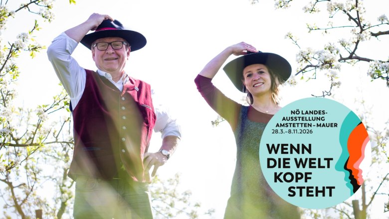 Zwei Personen mit Hüten in einem blühenden Garten, Plakat für NÖ Landesausstellung 2026.