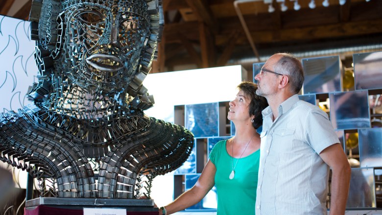 Zwei Personen betrachten eine gro&szlig;e Metallskulptur in einem Ausstellungsraum.