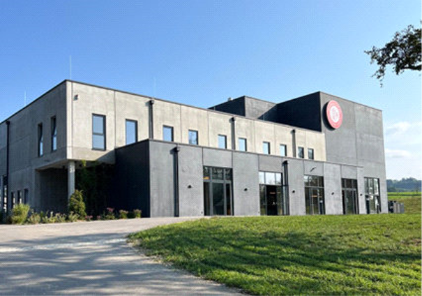 Modernes Gebäude der Destillerie Farthofer mit grauer Fassade und großen Fenstern, umgeben von grüner Wiese und blauem Himmel.
