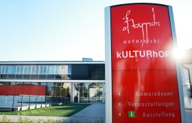 Ein modernes Gebäude mit Glasfassade und einem roten Schild mit der Aufschrift 'Ostarrichi Kulturhof'.
