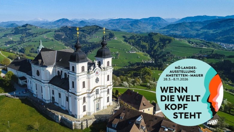Luftaufnahme der Basilika Sonntagberg mit umliegender Landschaft und einem Werbeplakat für die NÖ Landesausstellung 2026.