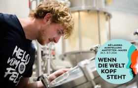 Ein Mann schaut in eine Brauanlage. Ein Logo der NÖ Landesausstellung 2026 ist eingeblendet.