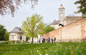 Gruppe von Menschen vor einer alten Burgmauer mit Turm im Hintergrund.