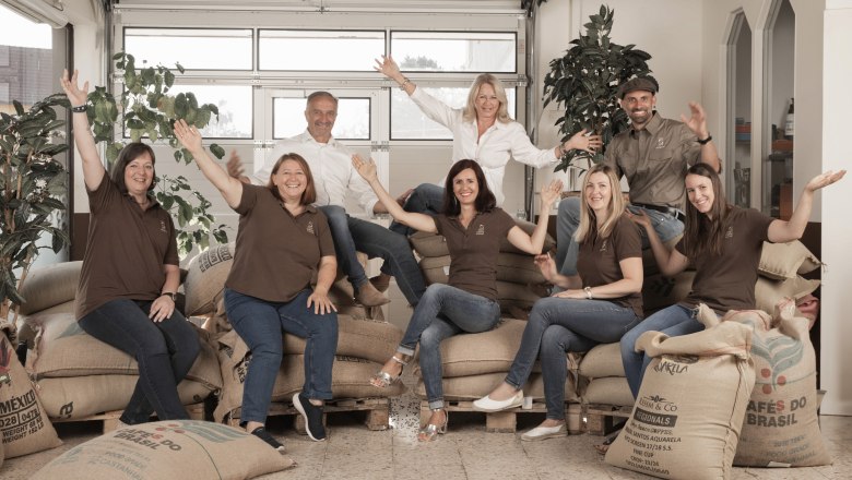 Eine Gruppe von Menschen sitzt auf Kaffees&auml;cken und l&auml;chelt in die Kamera.