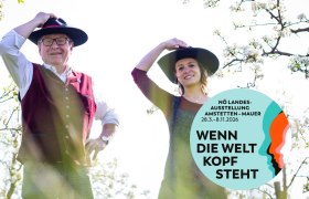 Zwei Personen mit H&uuml;ten in einem bl&uuml;henden Garten, Plakat f&uuml;r N&Ouml; Landesausstellung 2026.