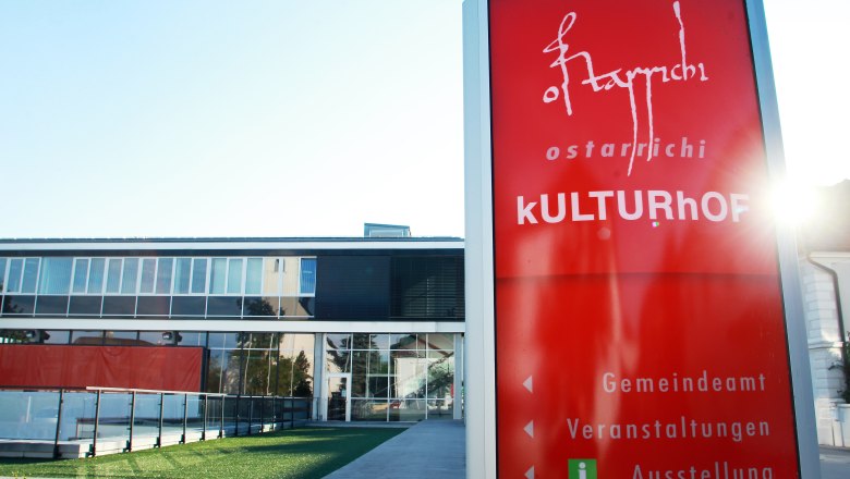 Ein modernes Gebäude mit Glasfassade und einem roten Schild mit der Aufschrift 'Ostarrichi Kulturhof'.